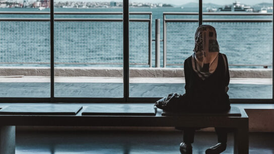 A female student is sitting on the bench and looking towards the sea.