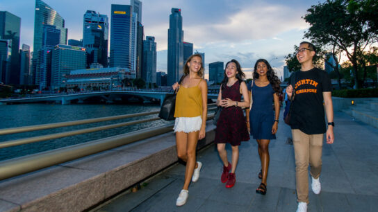 A boy and group of girls walking on the bank of the river.