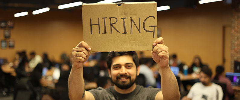 A man standing and holding hiring banner