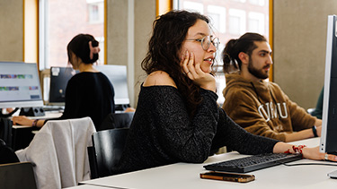 person sitting at desk using computer and resting face on hand