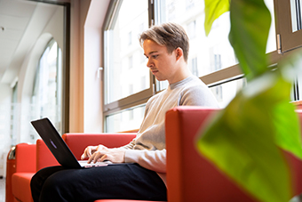 student sitting alone on campus and typing on laptop